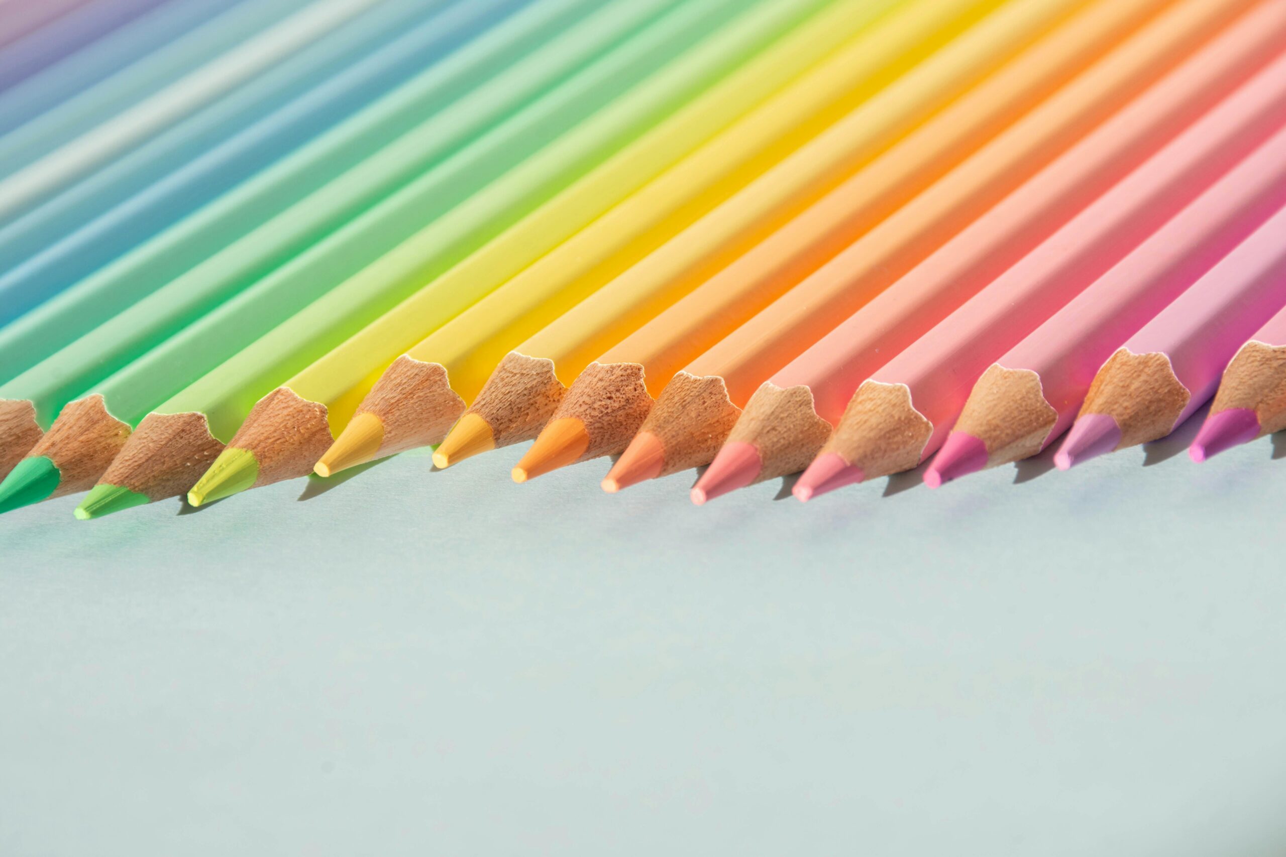 A close-up of colorful pencils arranged neatly, showcasing a rainbow gradient on a light background.
